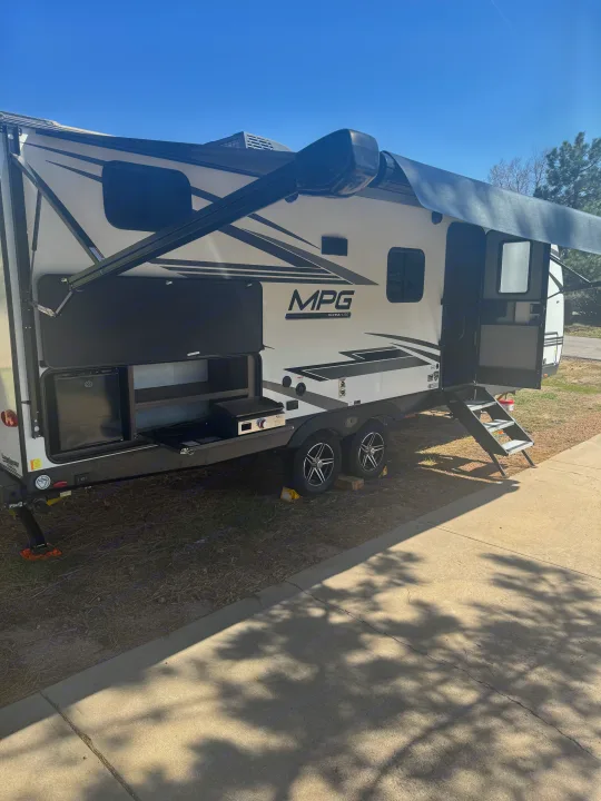View of a white MPG Ultra-Lite RV rental, showing its extended awning and outdoor kitchen with griddle.. Cruiser RV MPG 2500BH 2024
