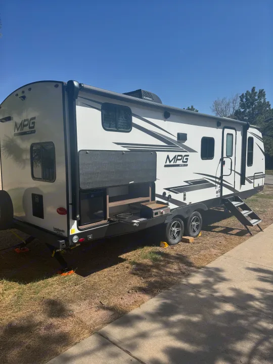 This white-and-black MPG Ultra-Lite RV rental is parked with its outdoor kitchen extended at a sunny site.. Cruiser RV MPG 2500BH 2024