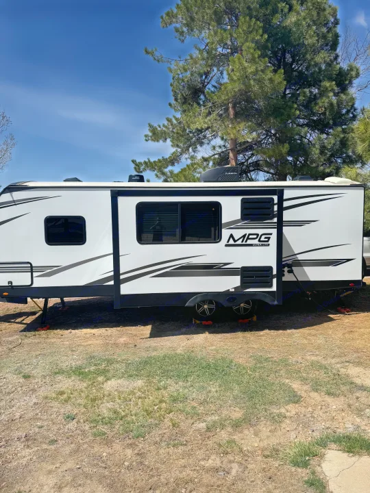 White MPG travel trailer, an RV rental, parked outdoors, set up at a sunny campsite under blue skies with trees.. Cruiser RV MPG 2500BH 2024