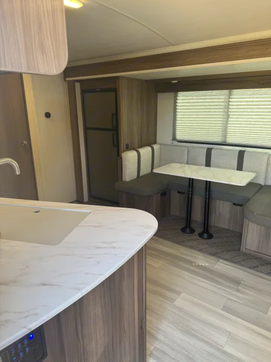 RV rental interior featuring a modern kitchen counter & a comfortable dinette with seating, table, & fridge.. Cruiser RV MPG 2500BH 2024