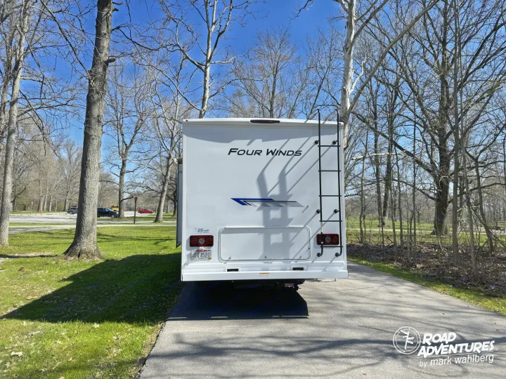 Back of a "Four Winds" RV rental parked in a sunny, tree-lined spot, ready for road adventures and camping.. Thor Motor Coach Four Winds 28Z 2026