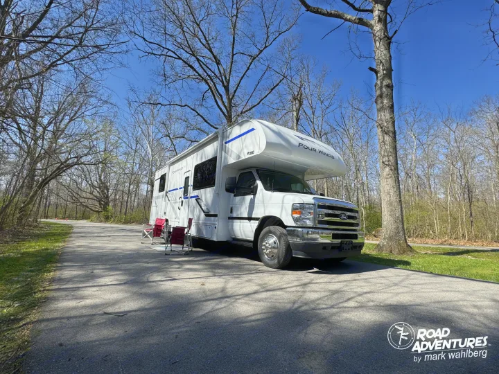This Four Winds **rv rental**, with red camping chairs, is parked in a sunny, wooded area for a road adventure.. Thor Motor Coach Four Winds 28Z 2026