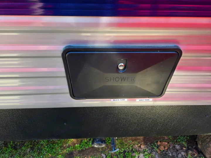 RV rental exterior: An outdoor shower utility panel is shown, with 'BLACK TANK' & 'GREY TANK' labels positioned below it.. Keystone RV Springdale 2023