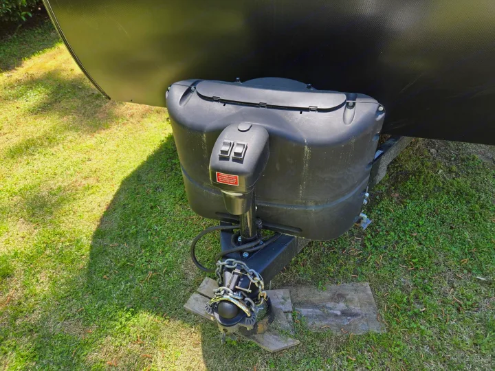 Black RV rental trailer's front hitch, featuring the power jack, safety chains, and propane tank cover.. Keystone RV Springdale 2023