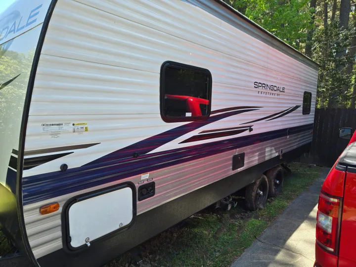 A white and blue Springdale travel trailer, ideal for an rv rental, parked outdoors next to a red truck on a sunny day.. Keystone RV Springdale 2023