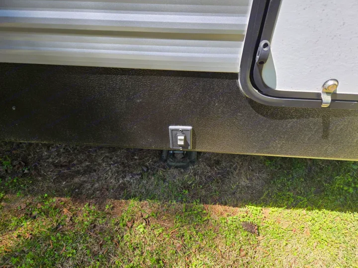 RV rental: Side of the travel trailer showing a power switch for electric stabilizer jacks (EXTEND/RETRACT) above grassy ground.. Keystone RV Springdale 2023