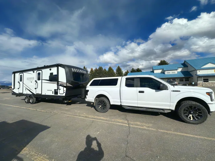 A white pickup truck is towing a black and white Rockwood travel trailer (an RV rental) in a paved lot under a cloudy sky.. Forest River Rockwood Ultra Lite 2024