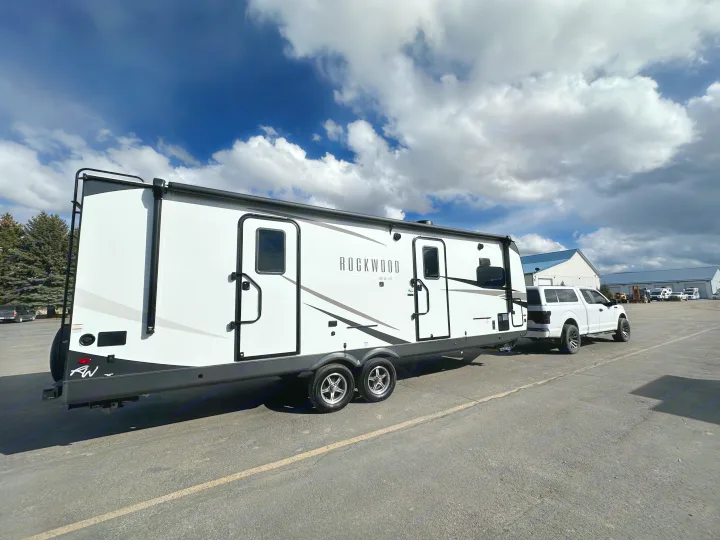 A white Rockwood travel trailer, hitched to a pickup truck in a sunny lot, is ready for your next RV rental adventure.. Forest River Rockwood Ultra Lite 2024