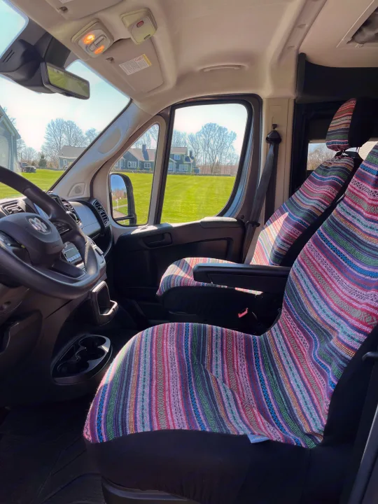 Bright RV rental interior: colorful striped seats, steering wheel, and sunny view of a green yard.. Pleasure-Way Pleasure-Way Class B 2022