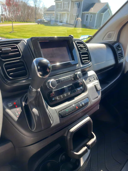 Interior view of an RV rental dashboard with gear shift and screen, offering a sunny view of a suburban neighborhood.. Pleasure-Way Pleasure-Way Class B 2022