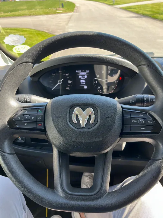 Driver's view inside an rv rental, showing the Ram steering wheel, dashboard with 405 mi trip, and the sunny road ahead.. Pleasure-Way Pleasure-Way Class B 2022