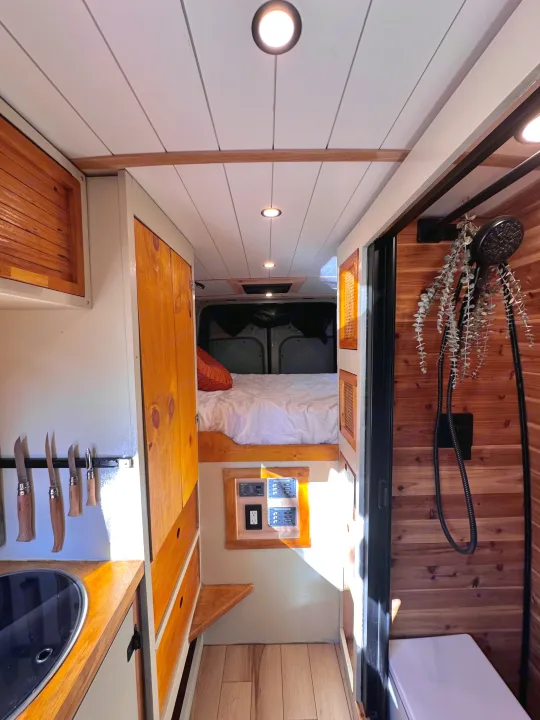 Inside a charming RV rental: full view of the compact kitchen, cozy bed area, and cedar-lined shower.. Mercedes-Benz Sprinter 2022