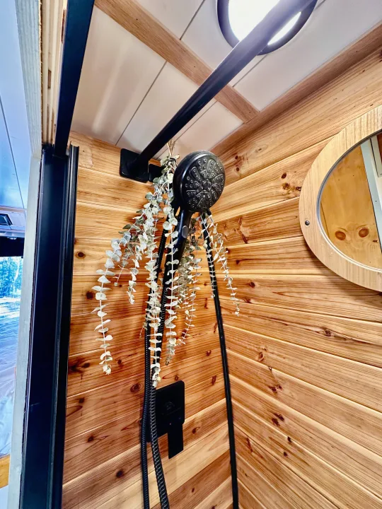 Experience our RV rental! Cozy shower with rustic wood walls, black fixtures, and decorative dried eucalyptus for a refreshing touch.. Mercedes-Benz Sprinter 2022