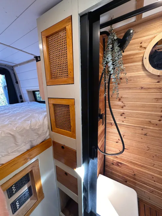 Cozy RV rental interior featuring a comfortable bed, custom rattan storage, and a modern shower with wooden walls.. Mercedes-Benz Sprinter 2022