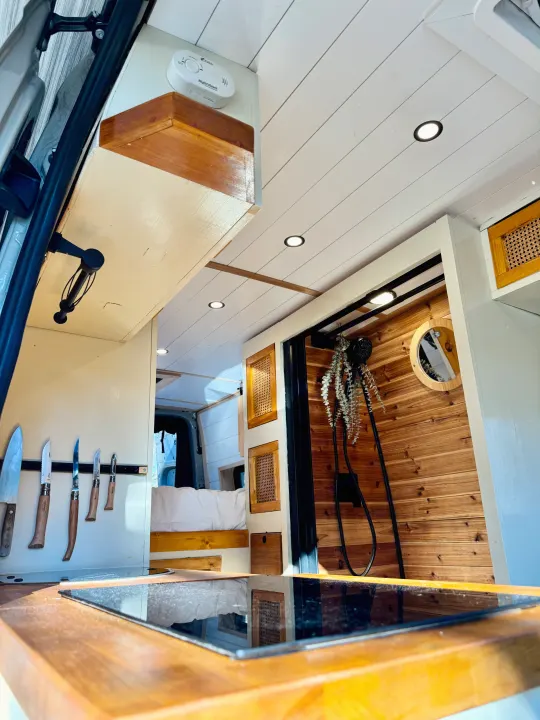 Custom RV rental interior featuring a smart kitchen with knives, a sleek shower, and cozy bed. Ideal for adventure.. Mercedes-Benz Sprinter 2022