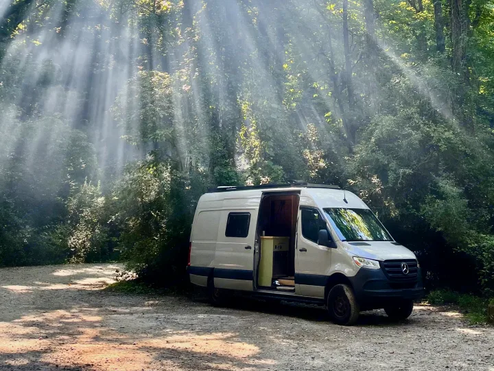 RV rental Sprinter van parked on a forest road, door open, bathed in stunning sunbeams & mist.. Mercedes-Benz Sprinter 2022