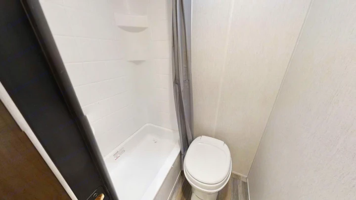 Compact RV rental bathroom features a white shower/tub, toilet, and grey curtain.. Forest River 17' Bunkhouse 2025
