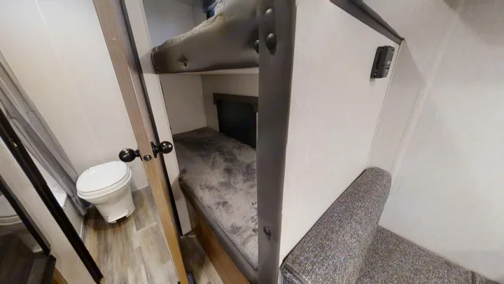 RV rental interior with functional bunk beds, a compact toilet in a small bathroom, and a grey upholstered bench.. Forest River 17' Bunkhouse 2025