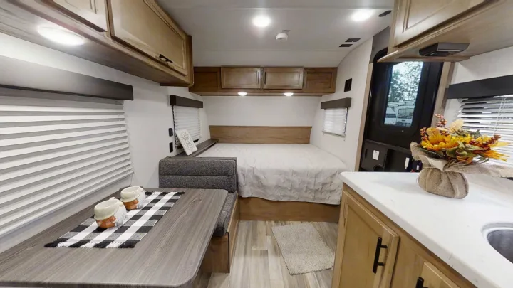 Cozy RV rental interior with a dining booth, full bed, and kitchen counter. Features wood accents and warm lighting.. Forest River 17' Bunkhouse 2025