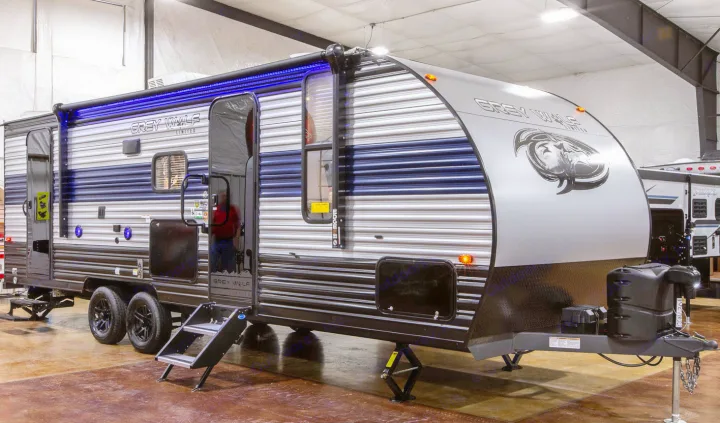 Grey Wolf travel trailer, an RV rental example, featuring blue LED awning lights and extended steps, displayed indoors.. Forest River 26' Bunkhouse with Slide 2025