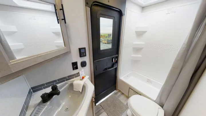 Compact RV rental bathroom interior: sink, mirror, toilet, shower/tub, and main door with exterior view.. Forest River 26' Bunkhouse with Slide 2025