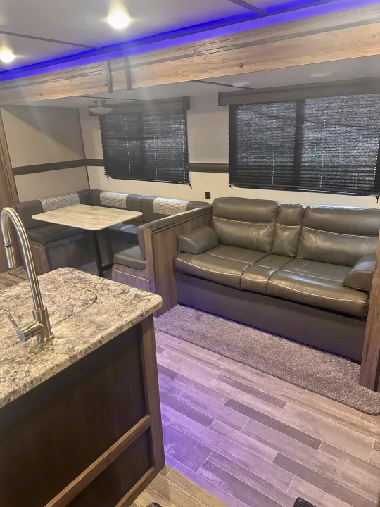 Spacious RV rental interior with dinette, sofa, island, and blue accent lighting, offering comfortable living space.. Crossroads RV Zinger 2020