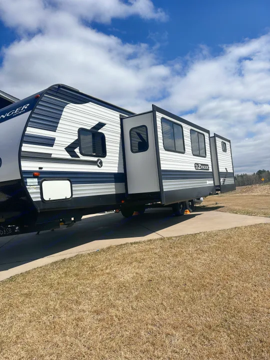 This RV rental, a Zinger travel trailer with extended slide-outs, is parked on a concrete pad under a blue sky, ready for camping.. Crossroads RV Zinger 2020