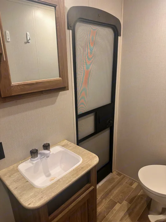 RV rental interior: A compact bathroom with a vanity sink, mirror, and view of the RV's screen entry door and toilet.. Crossroads RV Zinger 2020