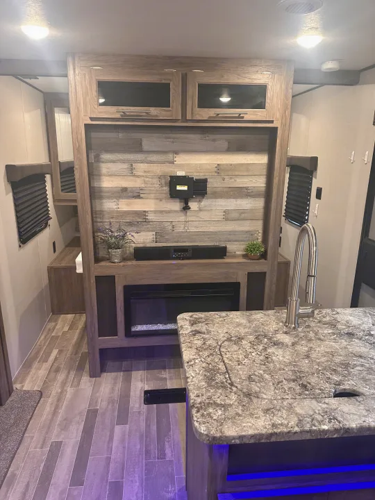 RV rental living area: modern entertainment center with fireplace, kitchen counter, and sleek blue under-lighting.. Crossroads RV Zinger 2020