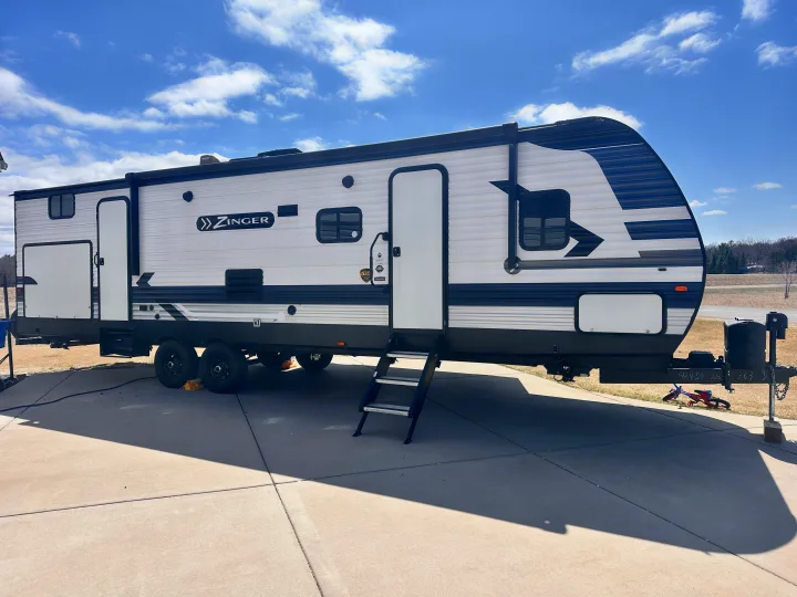 A spacious white & blue Zinger travel trailer, ideal for an RV rental. Parked on concrete under a bright, clear sky.. Crossroads RV Zinger 2020