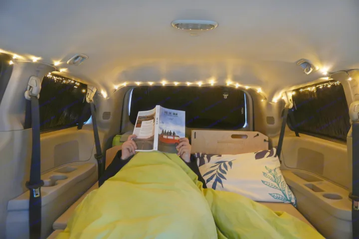 Person reads "Vie de Van" in a cozy RV rental, illuminated by warm string lights, showcasing comfortable van life.. Dodge Grand Caravan 2014