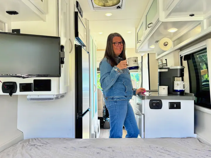 Woman enjoying coffee in her RV rental. Bright interior with modern kitchen, TV, and charging center.. Coachmen Beyond 2021