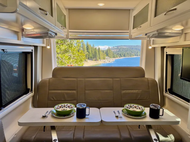 Enjoy a stunning lake and mountain view from this cozy RV rental dinette, perfectly set for a relaxing meal inside.. Coachmen Beyond 2021