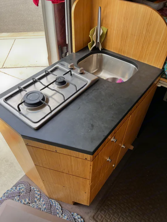 This RV rental features a compact kitchen with a two-burner stove, sink, black countertop, and bamboo cabinetry.. Ram promaster 2500 2017