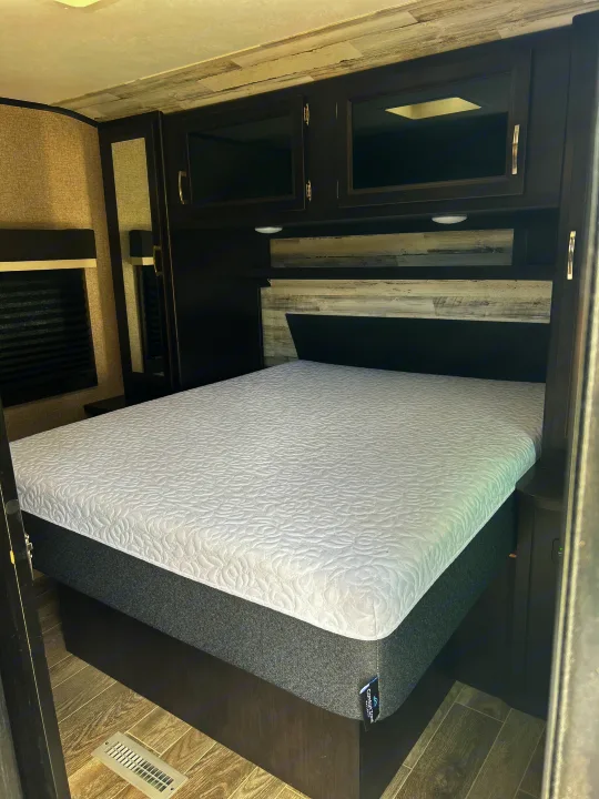 Cozy RV rental bedroom with a comfy ComfortZone mattress, dark cabinetry, and mirror, perfect for travel.. Jayco Jay Feather 2021