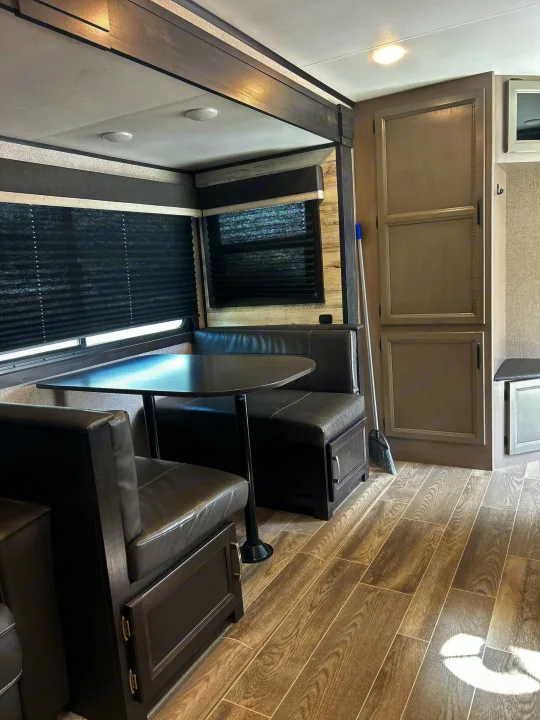 Clean RV rental interior showcasing a stylish dinette with dark benches and wood-look flooring for your journey.. Jayco Jay Feather 2021