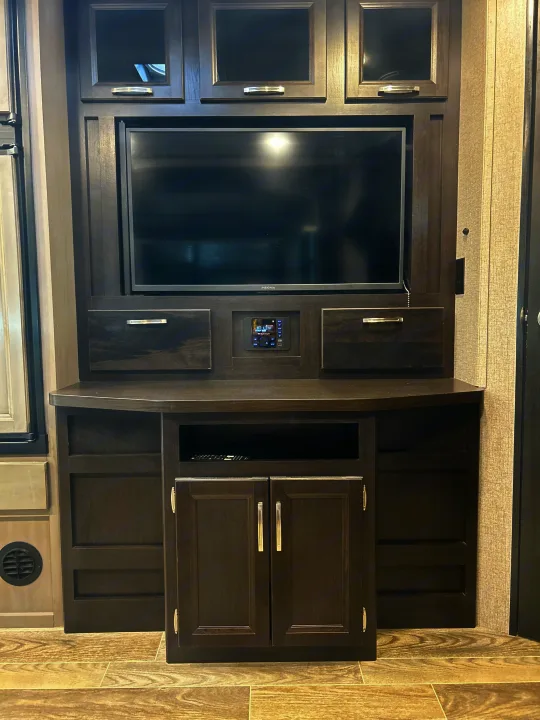 RV rental interior featuring a dark wood entertainment center with a large TV, control panel, & storage cabinets.. Jayco Jay Feather 2021