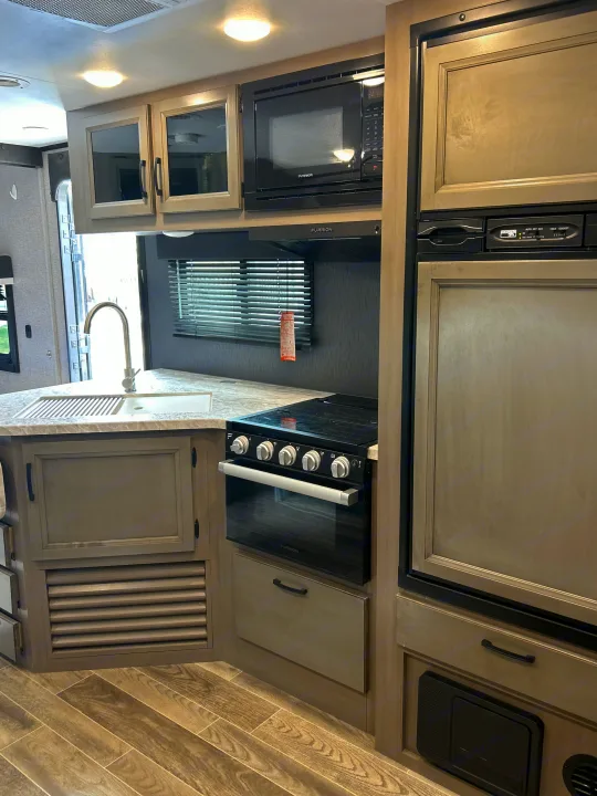 This RV rental kitchen features a sink, Furrion microwave, stove, and refrigerator, all within a modern, clean space.. Jayco Jay Feather 2021