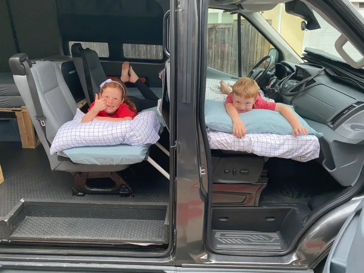 Happy kids relax on beds in an RV rental camper van. Great for family road trips & adventures!. Ford Transit 2016