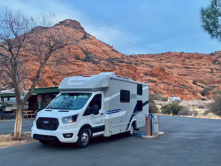 RV rental, a white & grey Coachmen Cross Trail, parked at a desert campground with red rock mountains.. Ford Transit 2023