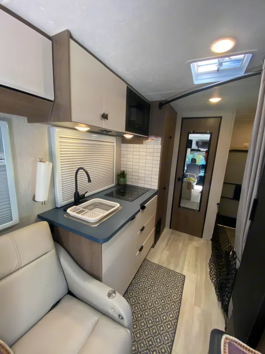 Clean rv rental interior features a modern kitchen with sink, induction cooktop, microwave, and cream seating.. Ford Transit 2023