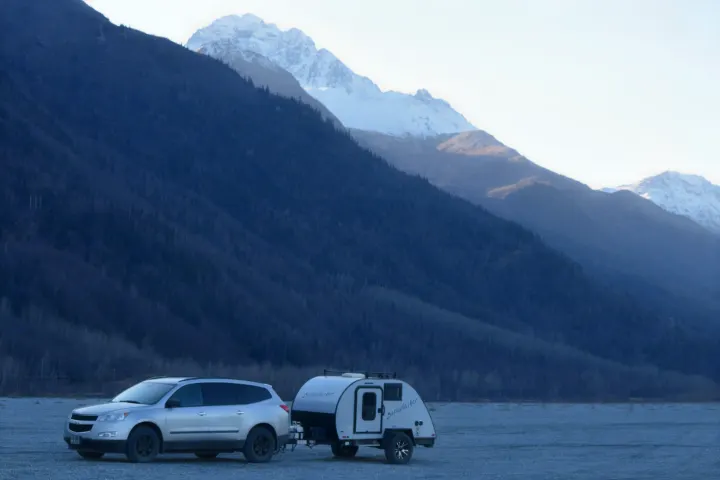 Silver SUV towing a Bushwhacker teardrop RV rental, parked among forested and snowy mountains.. Braxton Creek Bushwhacker 2022