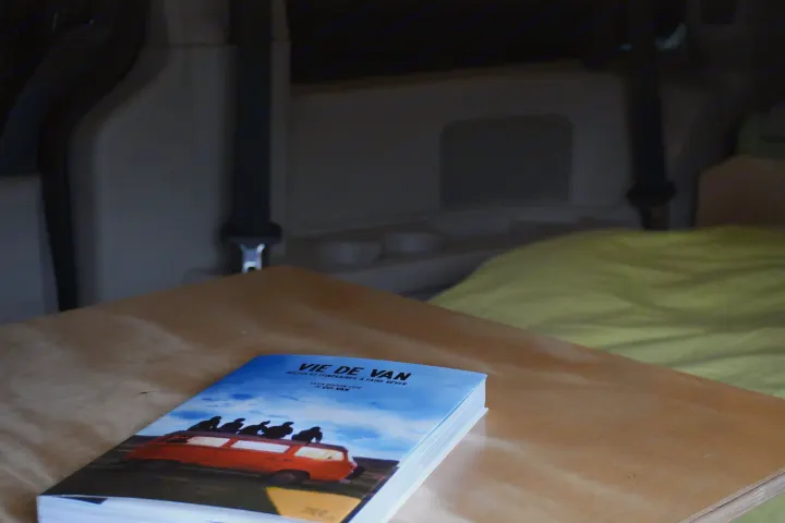 A book on "VIE DE VAN" (van life), featuring a camper van, rests on a wooden surface inside an RV. Great for rv rental adventures!. Dodge Grand Caravan 2014