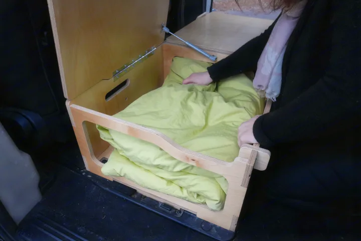 Efficient RV rental storage: Person places bedding in a custom wood pull-out drawer, part of a compact van setup.. Dodge Grand Caravan 2014
