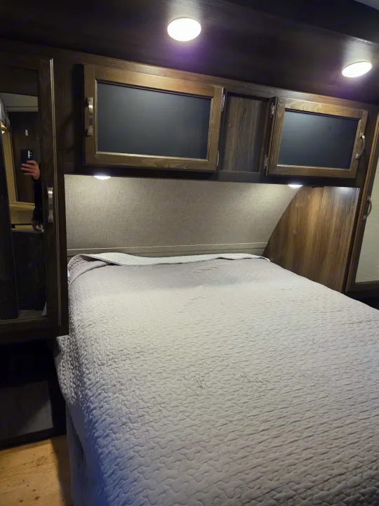 Explore this RV rental's bedroom: cozy bed, dark wood cabinets, and bright ceiling & reading lights.. Keystone RV Bullet Premier Ultra 2018