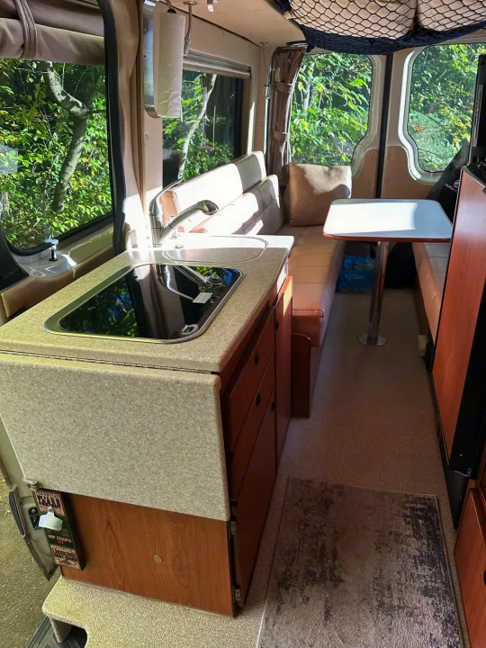 Explore this compact rv rental interior featuring a kitchenette, dining table, and cozy living space for travel.. Sportsmobile Regular Body 2013