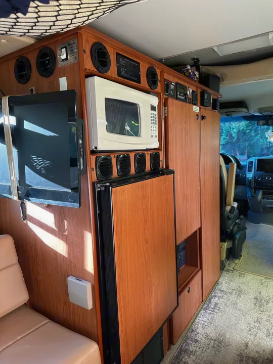RV rental interior: wood cabinetry with TV, microwave, refrigerator, and control panel for mobile comfort.. Sportsmobile Regular Body 2013