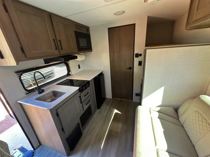 Bright RV rental interior showcasing a compact kitchen (sink, stovetop, microwave) and a comfortable sofa area.. Transcend One 2025 2025