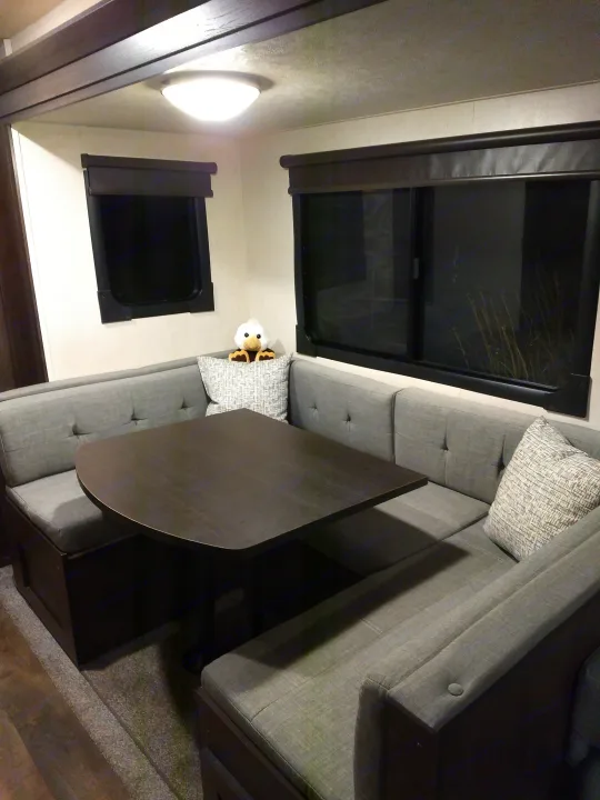 Interior of an RV rental showing a U-shaped dinette with grey cushions, a dark table, windows, and a plush toy.. Forest River Salem 2018