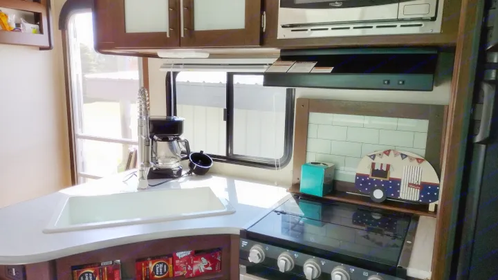 This rv rental shows a bright kitchen with a sink, stove, and microwave, offering a cozy interior for travel adventures.. Avenger ATI 2019